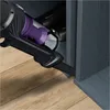A vacuum cleaner being used to clean a narrow gap next to a cabinet. Náhled obrázku produktu
