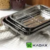 Two stainless steel roasting pans are stacked on top of each other, placed on a checkered cloth. In the background, jars of pasta and beans are visible. Voir les images du produit