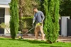 A man is using a string trimmer in a garden next to a house. Produktbild-Vorschau