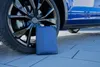 A folded blue car cover is placed on a paved surface next to the wheel of a blue car. Anteprima dell’immagine prodotto
