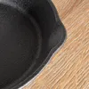 A close-up view of the edge of a black cast iron pan resting on a wooden surface. Produktbild-Vorschau