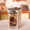 A person's hand is shown lifting the transparent cover of a miniature book nook designed to look like an arcade. Podgląd zdjęcia produktu