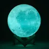 A glowing turquoise moon lamp on a wooden stand against a black background. Podgląd zdjęcia produktu