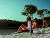 A couple sitting on a sandy beach next to two Aqua Marina BlueDrive X PRO Power Fin scooters. Podgląd zdjęcia produktu
