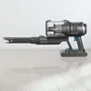 A cordless vacuum cleaner is shown on a light-colored wooden floor against a white wall. Podgląd zdjęcia produktu