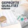 A close-up of a white quilted duvet with various certification tags and text overlays. Produktbild-Vorschau