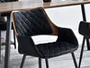 A close-up of a black upholstered dining chair with a wooden frame, placed near a wooden dining table. Náhled obrázku produktu
