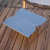 A foldable camping grill table made of metal is placed on a wooden surface. Náhled obrázku produktu
