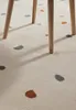 Close-up of a cream-colored rug with scattered multi-colored dots, under the legs of a wooden chair. Anteprima dell’immagine prodotto