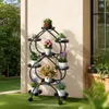 A black metal plant stand with multiple heart-shaped shelves holding various potted plants, placed on a green lawn next to a building. Náhled obrázku produktu