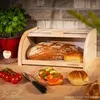 A wooden bread box filled with bread and rolls, with tomatoes and a sandwich on the side, on a wooden surface. Produktbild-Vorschau