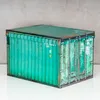 A green storage box designed to look like a shipping container, placed on a white surface against a gray concrete wall. Produktbild-Vorschau
