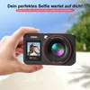 A hand holding a digital camera with a beach and palm trees in the background. Produktbild-Vorschau