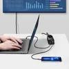 A person is using a laptop connected to a charger, which is also charging a smartphone. A large screen displaying charts is in the background. Anteprima dell’immagine prodotto
