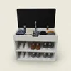 A white shoe cabinet with a black lid open, showing folded clothes and shoes on shelves. Produktbild-Vorschau