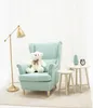 A teddy bear sits on a light blue armchair next to a floor lamp and small side tables. Voir les images du produit