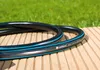 A black and blue garden hose is coiled on a wooden deck, with green grass in the background. Voir les images du produit
