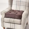A brown tufted seat cushion is placed on a plaid armchair. Náhled obrázku produktu