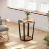 A round side table with a wood top and black metal legs, placed in a living room setting next to a rocking chair and near a window with sheer curtains. Podgląd zdjęcia produktu