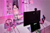 A gaming setup with a pink chair, monitor, laptop, headphones, and microphone, illuminated by pink LED lights. Produktbild-Vorschau