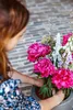 A woman arranging a bouquet of vibrant pink peonies and other flowers in a dark gray pot. Produktbild-Vorschau