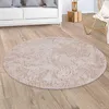 A round, shaggy rug is placed on a wooden floor in a living room setting, with a white sofa and a wicker chair visible in the background.