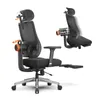 A black ergonomic office chair with a footrest is shown against a white background. The chair has adjustable features highlighted with orange accents and arrows. Náhled obrázku produktu