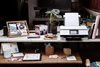 A home office desk setup with a printer, photos, plants, and stationery. Podgląd zdjęcia produktu
