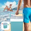 A person carrying a cooler on a beach with a woman relaxing in a chair in the background. Náhľad obrázku produktu