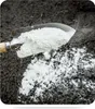 A garden trowel is scooping white powder fertilizer onto dark soil. Produktbild-Vorschau