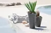 Two grey planters with plants are placed on a white gravel surface next to a pool of water. Náhľad obrázku produktu