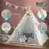 A child's play tent set up indoors, decorated with string lights and pillows. Podgląd zdjęcia produktu