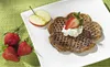 A plate of heart-shaped waffles with whipped cream and a strawberry, next to a sliced apple and whole strawberries on a green textured placemat. Produktbild-Vorschau