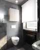 A modern bathroom with concrete-look walls, a wall-mounted toilet, a cabinet, and a window with blinds. Voir les images du produit