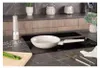 A kitchen counter with a frying pan on a stovetop, a salt grinder, and some asparagus on a cutting board. Produktbild-Vorschau
