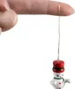 A finger holding a tiny snowman ornament by a golden thread. Náhled obrázku produktu