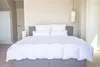 A neatly made bed with white bedding in a room with light-colored walls and doors. Produktbild-Vorschau