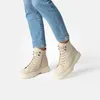 A pair of beige lace-up boots worn by a person in blue jeans. Produktbild-Vorschau