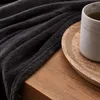 A close-up of a dark gray blanket draped over a wooden surface, with a mug of tea on a wooden tray. Anteprima dell’immagine prodotto