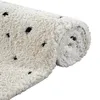 A rolled-up beige rug with black polka dots on a white background. Produktbild-Vorschau