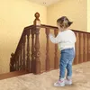 A toddler is standing next to a wooden staircase with a protective net installed on the railing. Náhľad obrázku produktu