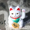 A white Maneki-neko (lucky cat) figurine with red ears and collar, a green bib, and a gold coin. Produktbild-Vorschau