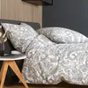 A neatly made bed with paisley patterned bedding, a bedside table with a laptop, and a vase with dried flowers. Produktbild-Vorschau