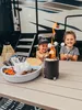 Two children are roasting marshmallows over a small portable fire pit on a picnic table, with an RV in the background. Voir les images du produit