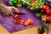 A person is chopping vegetables on a purple cutting board, with a salad and other ingredients in the background. Náhled obrázku produktu