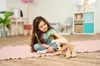 A young girl is playing with a stuffed dog on a pink rug in a room. Podgląd zdjęcia produktu