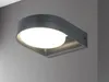 A modern gray outdoor wall light with a white illuminated diffuser, mounted on a light gray wall. Produktbild-Vorschau