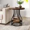 A round side table with a wooden top and black metal frame is placed next to a sofa in a living room setting. Produktbild-Vorschau