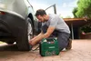 A man is using a portable air compressor to inflate a car tire outdoors. Produktbild-Vorschau