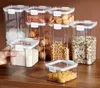 A collection of clear plastic food storage containers filled with various dry goods, arranged on a wooden surface. Produktbild-Vorschau